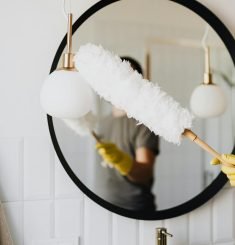 Photo by Photo By: Kaboompics.com Limpieza Abella Orteguerira Coruña A person cleaning an elegant bathroom mirror with a fluffy duster and yellow gloves.